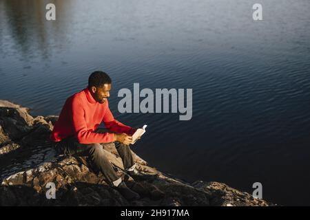 Man reading book while sitting on rock during weekend Stock Photo