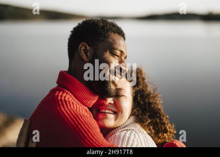Happy couple embracing by lake on sunny day Stock Photo