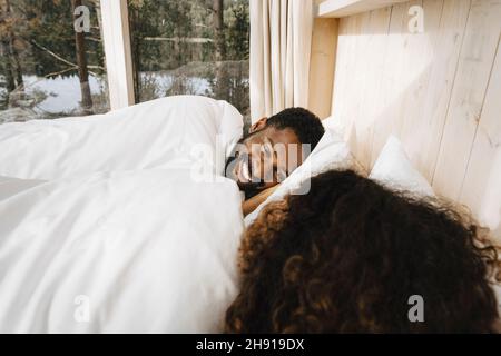 Happy man looking at girlfriend while lying on bed in hotel Stock Photo