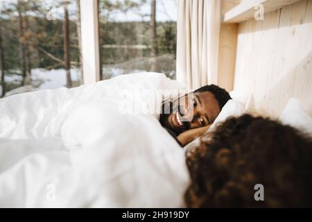 Smiling man lying with girlfriend on bed in cottage Stock Photo