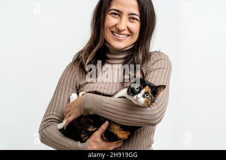 Close up photo of young adult woman smiling with domestic tabby cat on isolated background. Cat and pet lover concept. Stock Photo