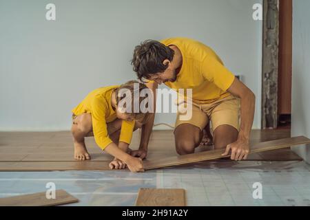 Father and son installing new wooden laminate flooring on a warm film floor. Infrared floor heating system under laminate floor Stock Photo