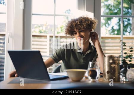 Smiling male teenager e-learning through laptop while doing homework at home Stock Photo