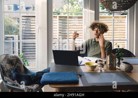 Teenage boy talking while studying through video call on laptop at home Stock Photo