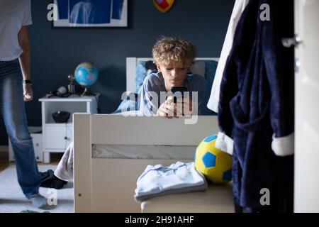 Boy using mobile phone while lying on bed at home Stock Photo