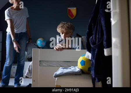 Mother scolding son using smart phone while lying on bed at home Stock Photo