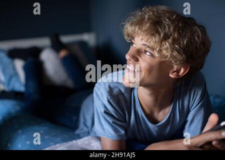 Blond boy smiling while lying on bed in bedroom at home Stock Photo
