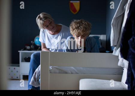 Mother looking at son using smart phone on bed in bedroom Stock Photo