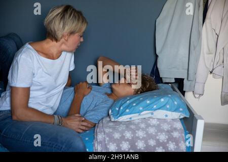 Blond woman talking with son lying on bed at home Stock Photo