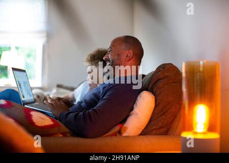 Smiling mature man using laptop while sitting by son on sofa in living room Stock Photo