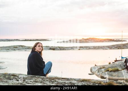 Woman looking over shoulder while sitting on island during sunset Stock Photo