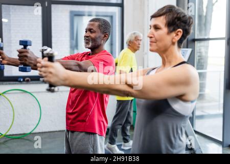 African american sportswoman exercising with dumbbells near senior sportswoman in sports center Stock Photo
