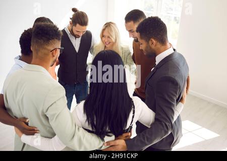 Diverse team of happy young business people standing in office and hugging each other Stock Photo
