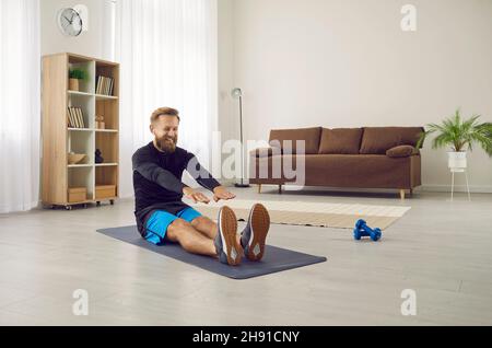 Happy sports man plays sports at home in morning and talks using wireless headphones. Stock Photo