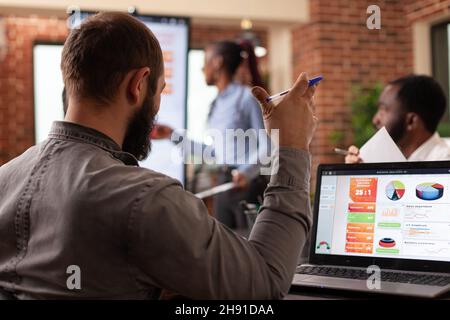 Businessman analyzing company graph on laptop computer working at management presentation during business meeting in startup office. Diverse businesspeople discussing collaboration project Stock Photo