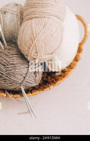 Natural wool in balls of various pastel colors in a wicker basket. Knitting threads close-up on a light background. Stock Photo