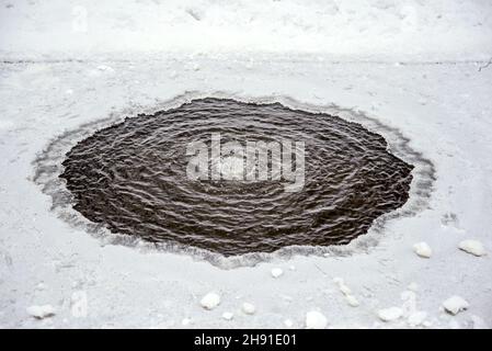 A round hole in the ice of a winter pond in a snow-covered park Stock Photo