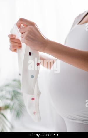 partial view of pregnant woman holding baby romper in bedroom Stock Photo