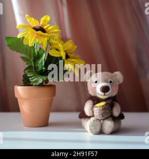 Toy hand-made cute bear sits with a barrel of honey next to the yellow flowers, felting wool Stock Photo