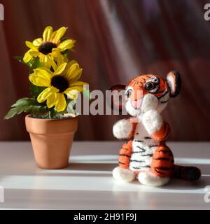 Cute toy tiger sitting next to yellow flowers, symbol of the year 2022, felting wool Stock Photo