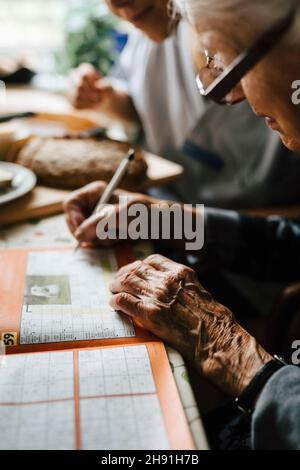 Senior woman solving crossword puzzle in book at table Stock Photo