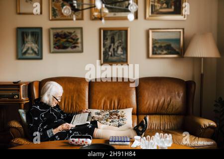 Senior woman reading newspaper while sitting on sofa in living room Stock Photo