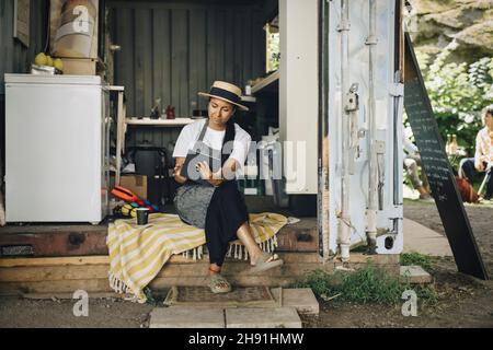 Female entrepreneur using digital tablet while sitting at doorway of food truck Stock Photo