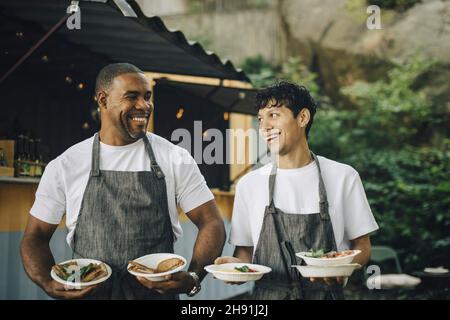 Happy male colleagues looking at each other with food by truck Stock Photo