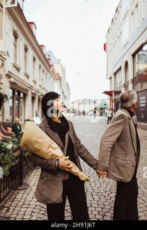 Elderly woman holding man's hand while walking on street in city Stock Photo