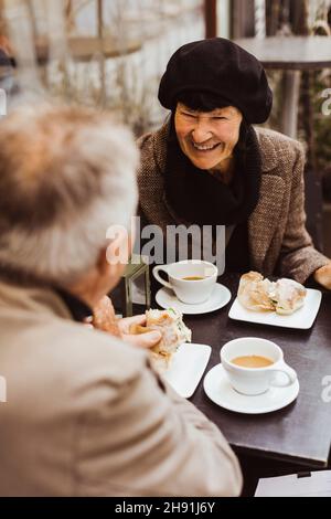 Smiling senior woman having breakfast with elderly man at sidewalk cafe Stock Photo