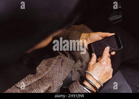 Directly above shot of senior woman using GPS navigation through smart phone in car during journey Stock Photo