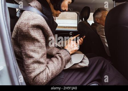 Senior woman using smart phone while traveling with man in car Stock Photo