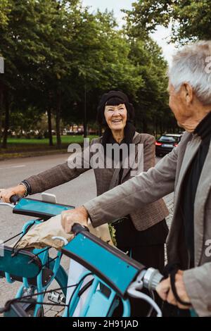 Smiling senior couple with electric bicycles on street Stock Photo