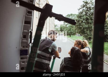 Delivery man sharing smart phone with female coworkers Stock Photo