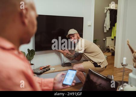 Smiling male technician looking at mature man using smart phone in living room Stock Photo