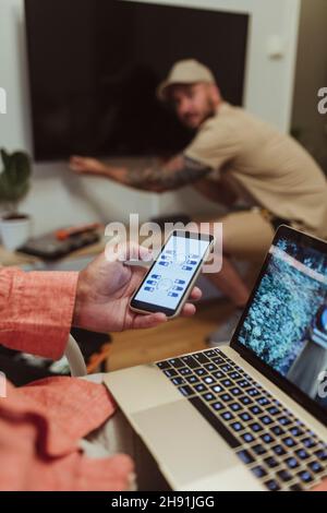 Mature man using smart phone while male blue-collar worker fixing television set at home Stock Photo