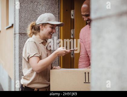 Smiling female worker taking photo of package while delivering to male customer Stock Photo