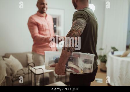 Male craftsperson holding toolbox while doing handshake with customer at home Stock Photo