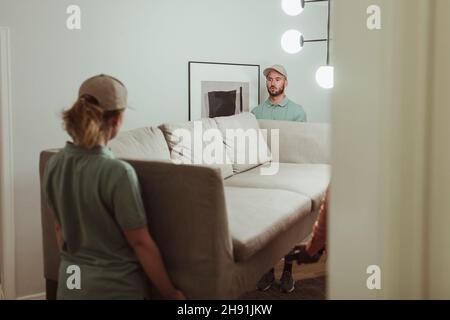 Male and female coworkers carrying sofa at home Stock Photo