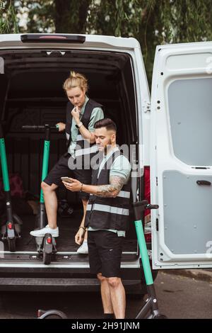 Delivery man sharing smart phone with female coworker in van Stock Photo