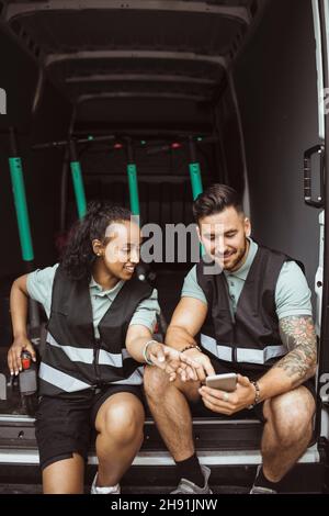 Smiling female and male coworkers using smart phone while sitting in delivery van Stock Photo
