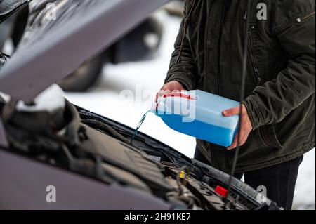 driver refilling the blue non-freezing windshield washer liquid in the tank of the car, closeup Stock Photo