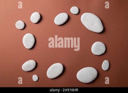 Flat lay view of frame made with flat smooth sea stones on tranquil brown background. Minimalist products background set. Stock Photo