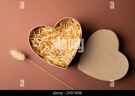 Top view of natural color open heart shape cardboard box with shredded wood excelsior for filling inside, pastel brown background. Natural sustainable Stock Photo