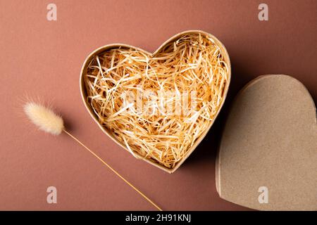 Top view of natural color open heart shape cardboard box with shredded wood excelsior for filling inside, pastel brown background. Natural sustainable Stock Photo