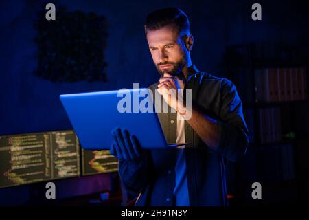 Photo of minded pensive guy arm on chin serious face look netbook project start-up late evening dark room Stock Photo