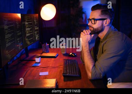 Profile portrait of minded clever guy arms on chin look two displays creative contemplate late evening indoors Stock Photo
