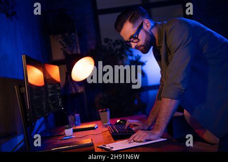 Profile photo of serious skilled guy read papers write email keyboard create project dark night office Stock Photo