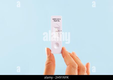 Woman holding COVID-19 coronavirus antigen rapid test over blue background. Selftesting at home. Stock Photo