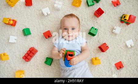 Portrait of smiling baby boy surrounded with lots of toys lying on carpet in playroom. Concept of children development, education and creativity at Stock Photo